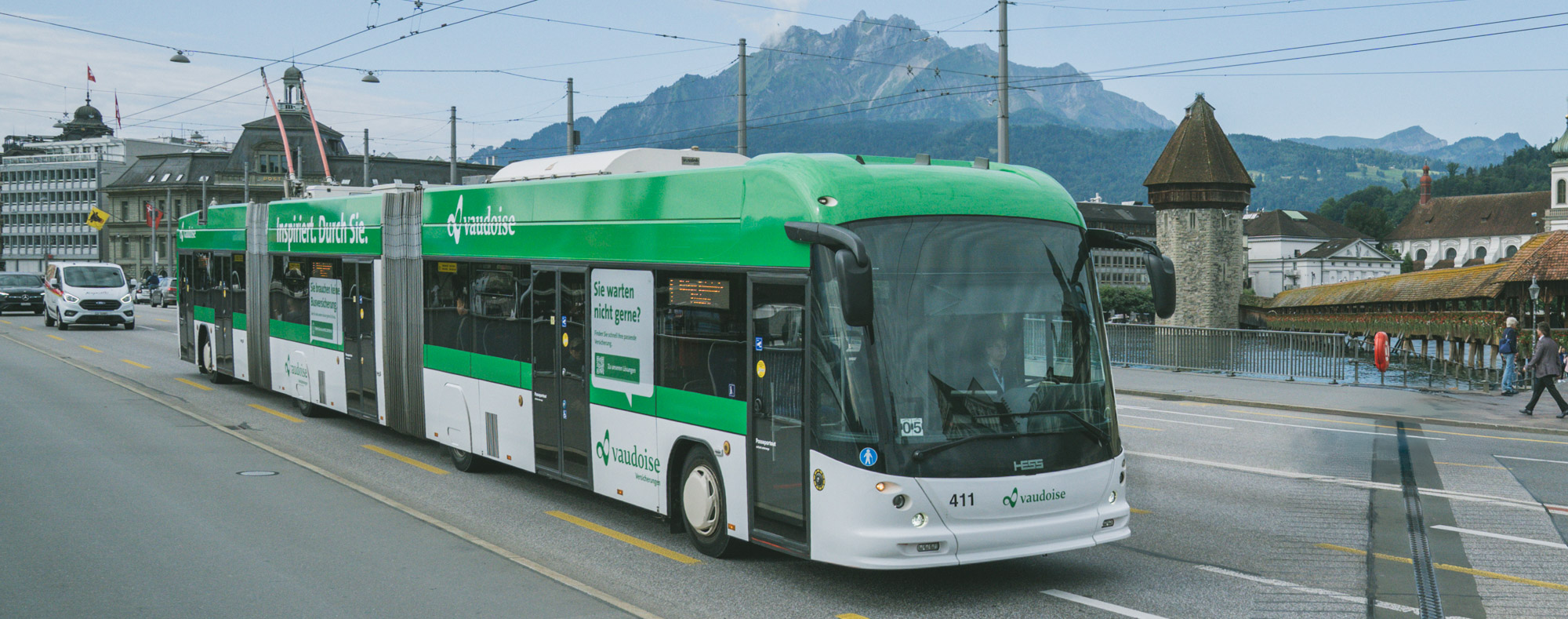 Doppelgelenktrolleybus der Verkehrsbetriebe Luzern mit Vaudoise-Werbung fährt über die Seebrücke in Luzern, im Hintergrund Kapellbrücke, Wasserturm und Pilatus.