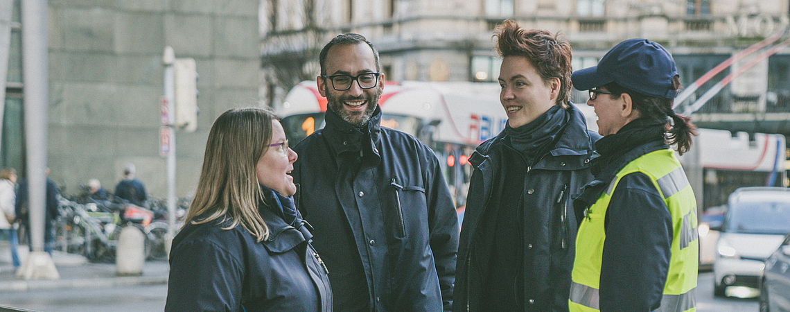 Vier Mitarbeitende der Verkehrsbetriebe Luzern in Arbeitskleidung unterhalten sich an der Haltekante B am Bahnhof Luzern.