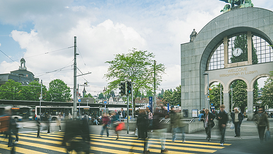 Belebter Bahnhofplatz Luzern mit VBL-Bussen und dem Torbogen im Hintergrund.